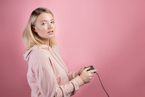 A young blonde girl who is passionate about the game uses a gamepad - Foto, imagen