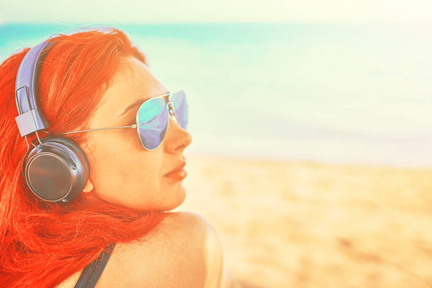 Piękna kobieta w okularach przeciwsłonecznych słuchająca muzyki na plaży. - Zdjęcie, obraz