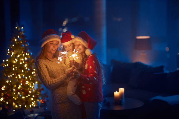 Mother and two daughters using sparklers near christmas tree - Fotografie, Obrázek