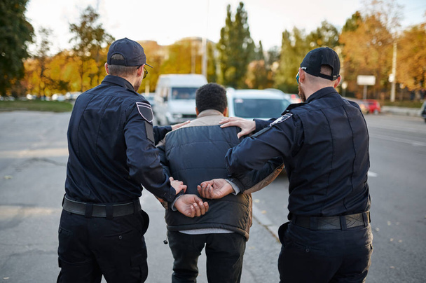 Двое полицейских мужчин арестовывают молодого человека - Фото, изображение