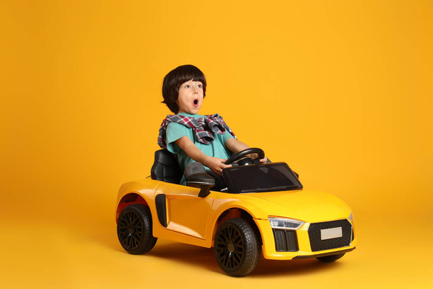 Little child driving toy car on yellow background - Foto, imagen