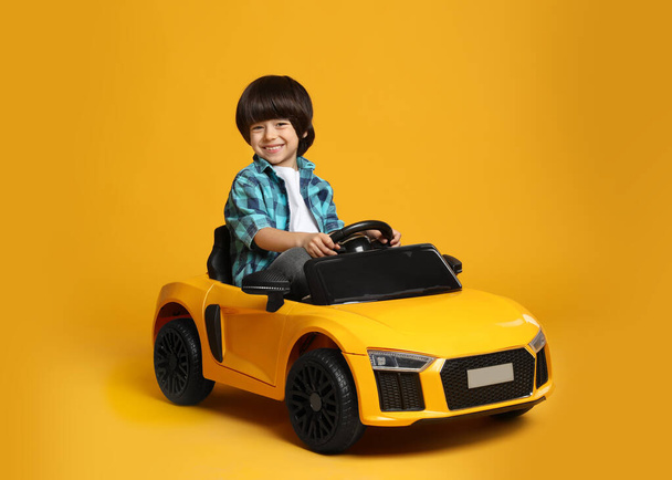 Cute little boy driving children's electric toy car on yellow background - Foto, Imagem