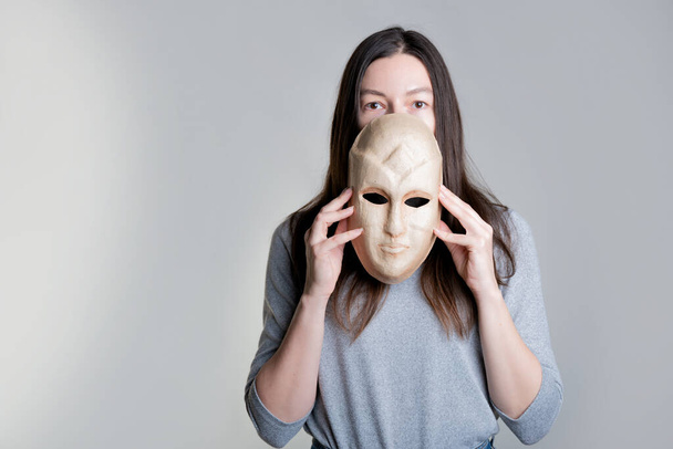 A young woman hides her face behind a mask, the concept of psychological problems, - Foto, Bild