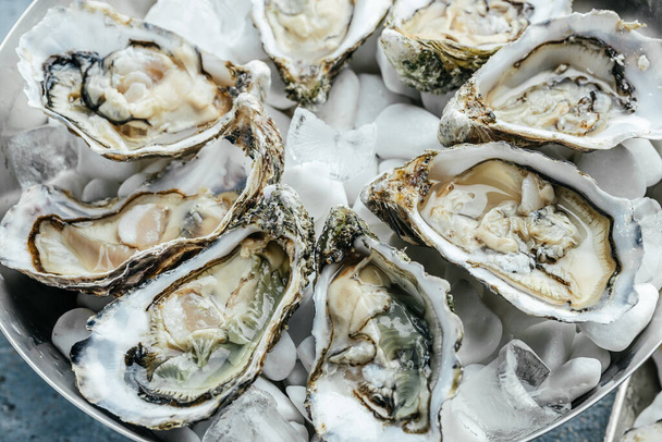 many kinds opened oysters in a plate with ice and lemon on blue background, Healthy food, gourmet food. Oyster dinner in restaurant. top view, - Фото, зображення