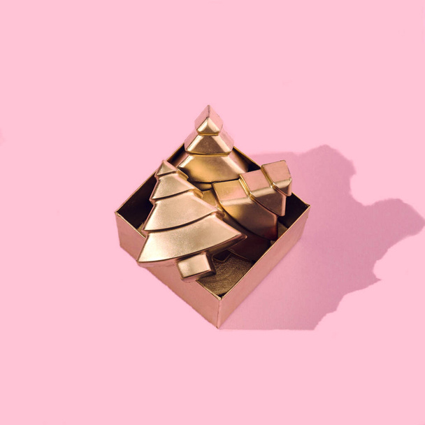 Uma caixa dourada com árvores de Natal mínimas geométricas douradas sobre fundo rosa. Conceito criativo moderno brilhante para o convite do partido da véspera do Natal ou do Ano Novo. - Foto, Imagem