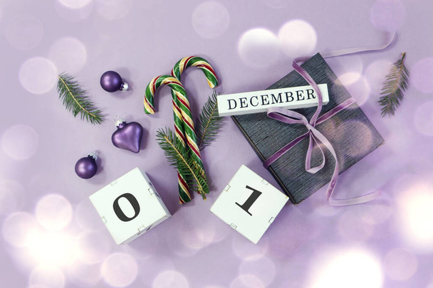 Calendar for December 1: name of the month in English, numbers on cubes 0 and 1, Christmas tree decorations, holiday caramel, padarok tied with a pastel ribbon on a pastel background, top view, bokeh - Valokuva, kuva