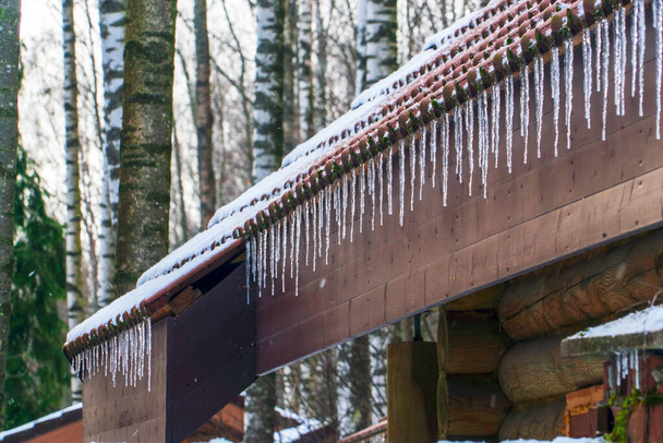 Eiszapfen und Schnee auf dem Dach eines Holzhauses. Winterlandschaft. Gebiet Leningrad - Foto, Bild