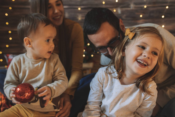 Young parenthood. Hispanic family laughing with their baby and daughter in living room decorated by christmas tree. Portrait of loving family holiday. Merry xmas and Happy New Year. - Fotoğraf, Görsel