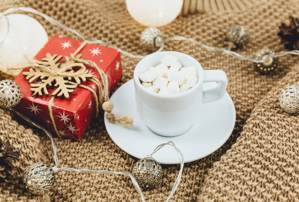 Eine Tasse Kaffee, brauner Strickpullover und Girlanden, LED-Lichter. Frauen tragen Winterbekleidung und Accessoires. Neujahrs- und Weihnachtsfeier-Attrappe. Weihnachtsstillleben - Foto, Bild