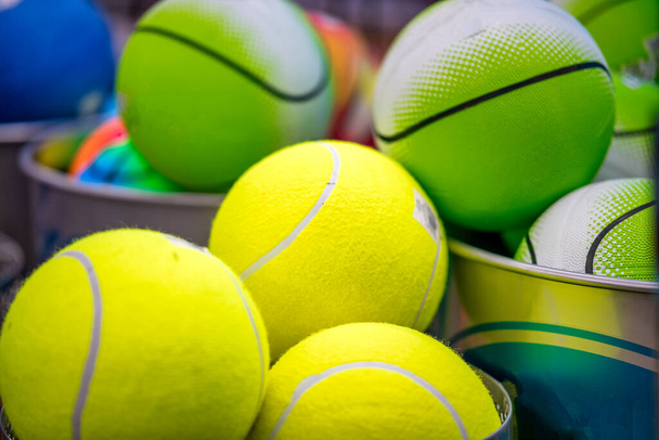 Sarı tenis topları ve kovadaki yeşil basket topları, spor konsepti. - Fotoğraf, Görsel
