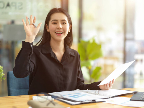 Friendly young business woman smiling and saying hi to her colleagues, hello, greeting hand sign, welcoming her freinds. - Foto, Imagem