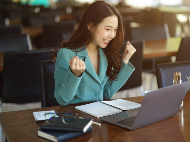 Erfolgreiche Geschäftsfrau, weibliche Angestellte, die mit erhobener Hand feiert, während sie auf den Laptop schaut. Aufgeregt, extrem glücklich. - Foto, Bild