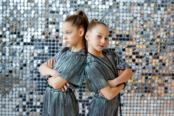 Due ragazze adolescenti in piedi con le spalle l'una all'altra in argento tute futuristiche sullo sfondo di una parete iridescente d'argento. - Foto, immagini