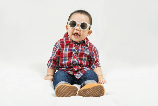 Cute 6-7 months little asian baby boy in casual outfit and baby boots sitting on white blanket cool and happily at home,Stylish fashionable kid. Adorable child in fashion and Style. - Fotó, kép