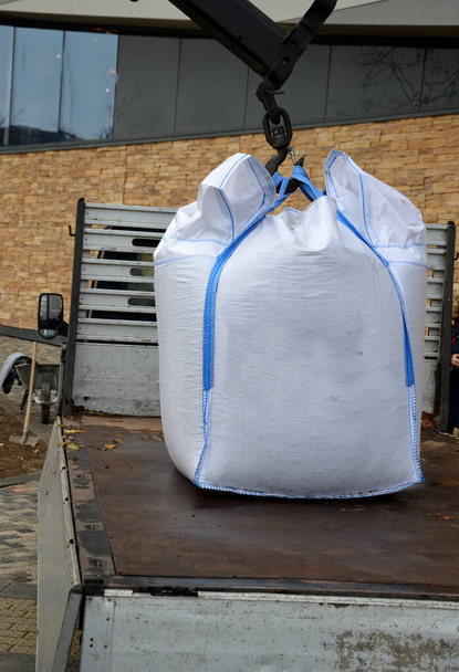 carregando grandes sacos de plástico brancos cheios de substrato de cobertura em um caminhão menor. guindaste segurando no ar um metro cúbico de cascalho pesado pelas alças no gancho. - Foto, Imagem
