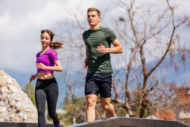 Sport couple run together in park. Young people jogging together at fitness training outdoor. Man and woman at sport training together - 写真・画像