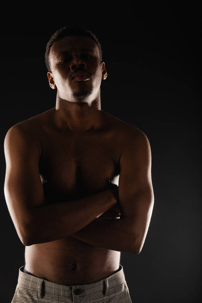 Handsome black male is posing while flexing on black background - Fotó, kép