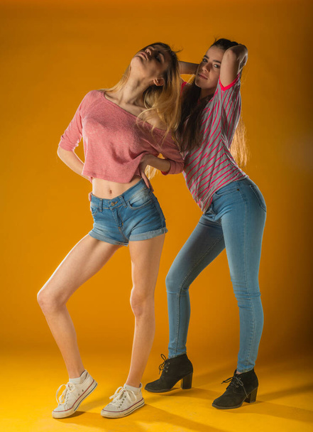 Romantic female friends in trendy clothes standing on yellow background. Carefree girls sending air kisses. - Photo, Image