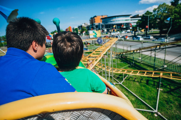 tiener en zijn kleine broer rijden in een achtbaan in een pretpark - Foto, afbeelding
