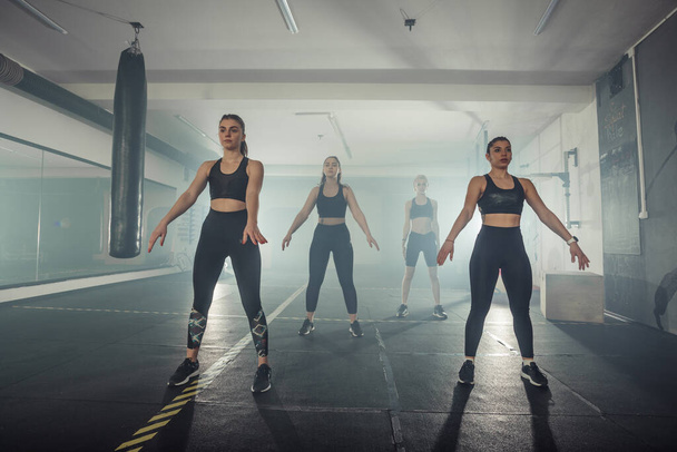 Vier junge Sportlerinnen machen Kniebeugen im trendigen Sportoutfit. - Foto, Bild