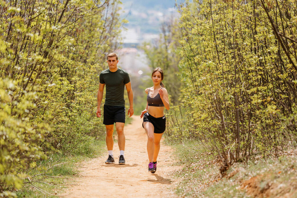 Homme et femme faisant de l'exercice et faisant du jogging ensemble au parc. Heureux et souriant comme ils courent le long du chemin pendant le coucher du soleil par une chaude journée d'été - Photo, image