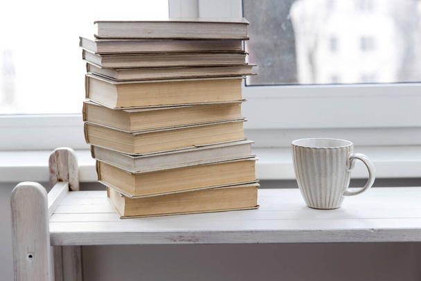 A stack of white-bound books is on the table against the background of the window. The cup of tea is next to books. School education concept. - Foto, immagini