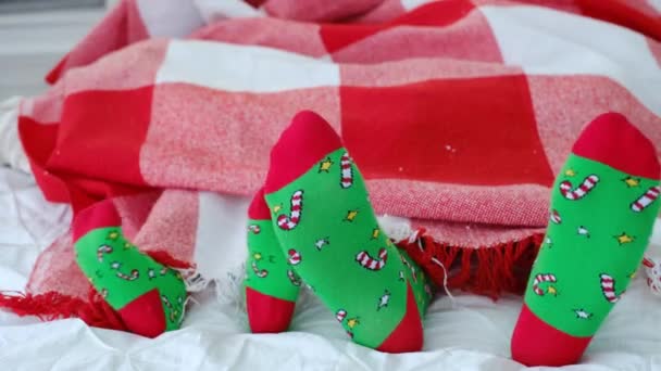 Papa en dochter in identieke groene sokken met een kerstdecor met suikerriet en sterren. Een volwassene rust met een kind in een gezellig warm bed. Voeten groot en klein close-up. Nieuwjaarskousen - Video