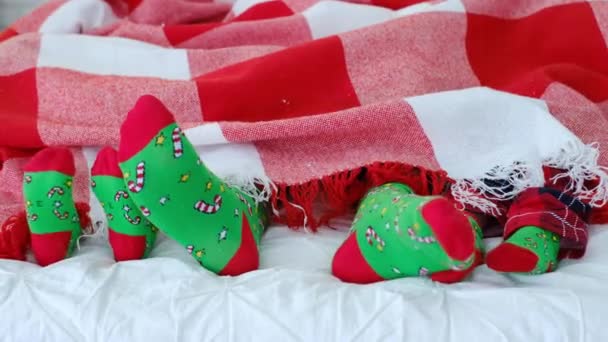 Vader en zijn kinderen genieten van een rust liggend in bed in identieke rode en groene sokken met een ornament van kerstlolly 's. Warme deken en een comfortabel bed. Wol geruit in een kooi. thuishaard - Video