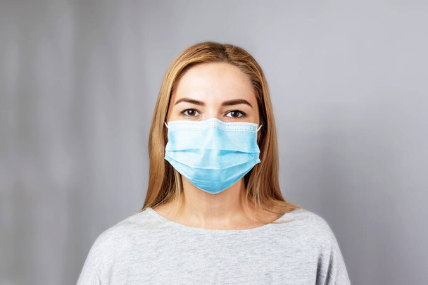 Stop virale infectie. Meisje met een masker op een grijze achtergrond. Meisje met een medisch beschermend masker op een grijze achtergrond. Het concept van bescherming tegen virussen en ziektekiemen op openbare plaatsen. - Foto, afbeelding