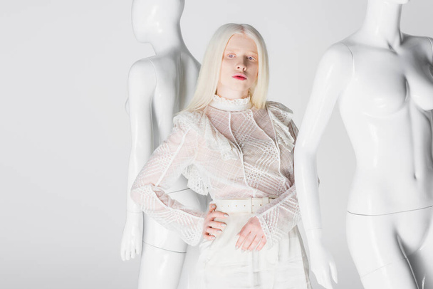 Mladý albín žena v blůze drží ruku na boku poblíž figurín izolované na bílém  - Fotografie, Obrázek