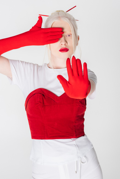 Trendy albino model in gloves and red lips showing stop gesture isolated on white - Фото, зображення