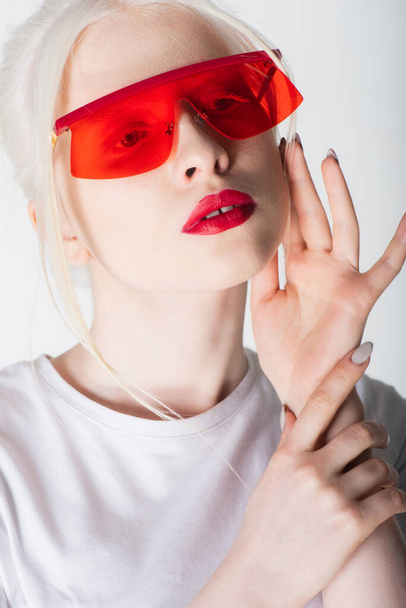 Portrait of albino model in red sunglasses touching face isolated on white - Φωτογραφία, εικόνα