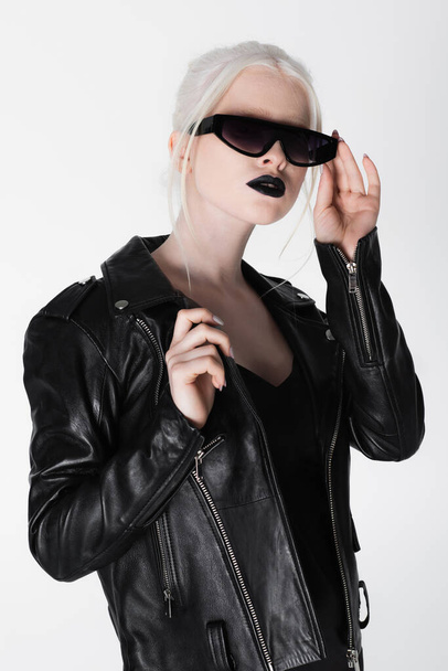 Stylish albino woman in leather jacket holding sunglasses isolated on white - Zdjęcie, obraz