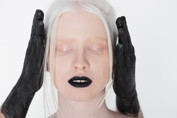 Male hands in black paint covering ears of albino model isolated on white - Photo, Image