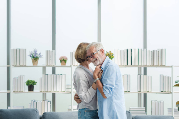 Ηλικιωμένοι ηλικιωμένοι ζευγάρι της οικογένειας σε casual στολή αγκαλιάζει μαζί με χαμόγελο ευτυχισμένη και ρομαντική συγκίνηση στο σαλόνι. - Φωτογραφία, εικόνα