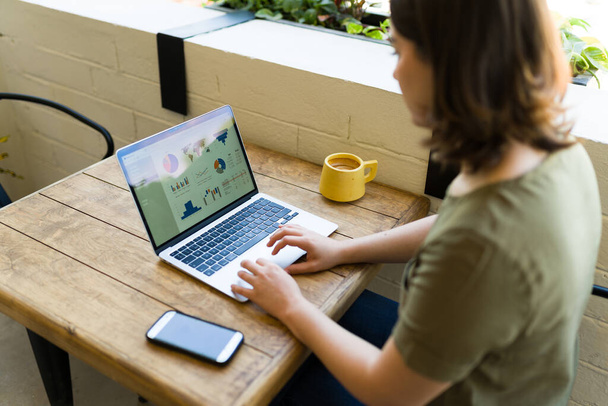 Rückansicht einer jungen Frau, die freiberuflich am Laptop arbeitet, während sie draußen im Café sitzt - Foto, Bild