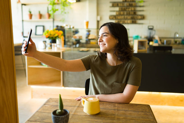 Onnellinen asiakas ottaa selfie hänen älypuhelin odottaessaan hänen tilauksensa kahvilassa - Valokuva, kuva