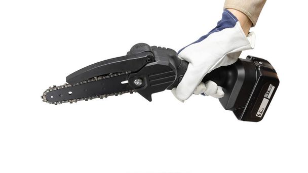 La mano en el guante sostiene la motosierra eléctrica portátil con batería, herramienta para trabajar con madera, primer plano aislado sobre fondo blanco - Foto, imagen