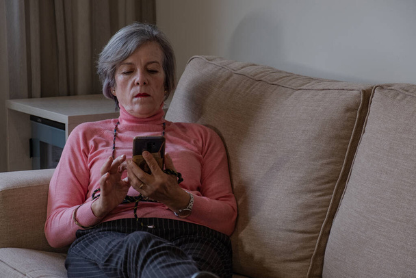 mujer madura acostada en un sofá revisando su teléfono celular - Foto, Imagen