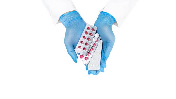 青い医療用手袋の手は、白い背景に隔離された薬を保持しています.クローズアップビュー.薬局バナー.医薬品や薬や錠剤の利点.薬局のバナー。手は心のジェスチャーを示しています。医療の概念 - 写真・画像