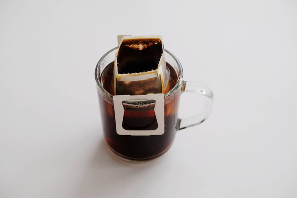 Tropfbeutel Kaffee auf Glasschale vorhanden. Sofortige, frisch gebraute Methode. Weißer Tisch - Foto, Bild