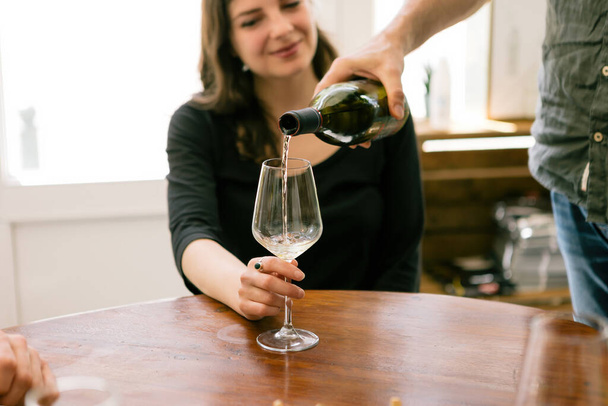 mano dell'uomo versando vino bianco nel bicchiere - cliente femminile che tiene il bicchiere di vino al tavolo del caffè - Foto, immagini