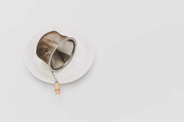 a white plate with tea metal filter and tea leaves inside on a white background - Φωτογραφία, εικόνα