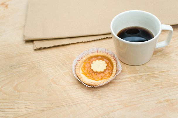 black coffee cup and sweet jam cupcake on a wood and brown paper tabletop background with text space - Photo, Image