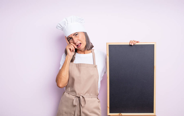 senior pretty woman feeling bored, frustrated and sleepy after a tiresome. chef and blackboard concept - Foto, imagen