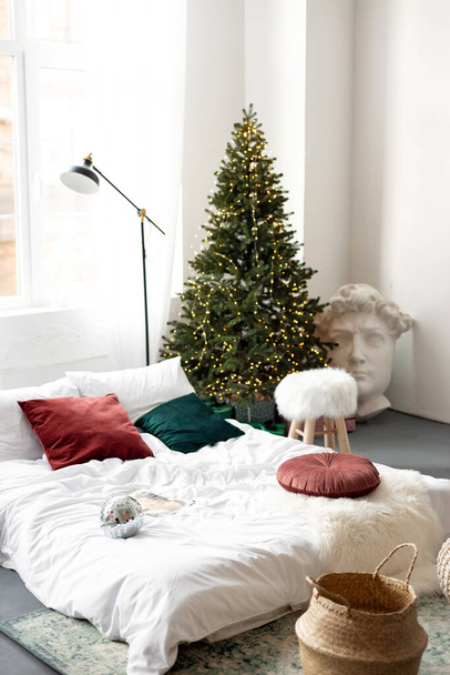 Karácsonyi dekoráció. Hálószoba világos színekben egy nagy ágy. A belső tér díszített koszorúk, karácsonyi koszorúk és egy újévi fa modern stílusban. Puha szelektív fókusz. - Fotó, kép