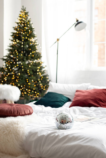 Karácsonyi dekoráció. Hálószoba világos színekben egy nagy ágy. A belső tér díszített koszorúk, karácsonyi koszorúk és egy újévi fa modern stílusban. Puha szelektív fókusz. - Fotó, kép