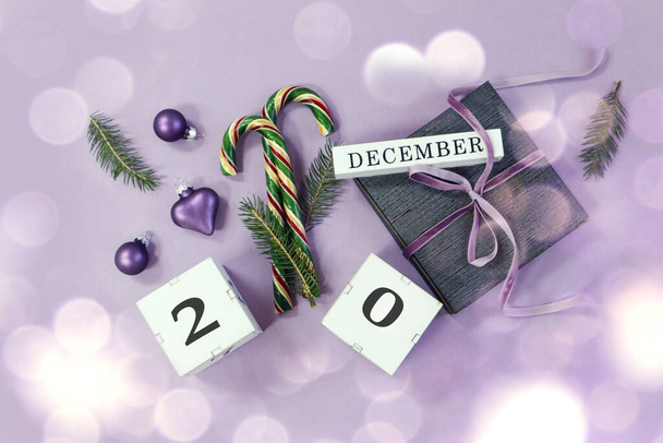 Calendar for December 20: the name of the month in English, the number 20 on the cubes, Christmas decorations, festive caramel, padarok tied with a pastel ribbon on a pastel background, top view, bokeh - Photo, image