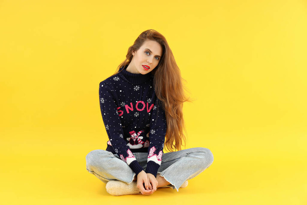 Attraktive junge Frau im Weihnachtspullover auf gelbem Hintergrund - Foto, Bild