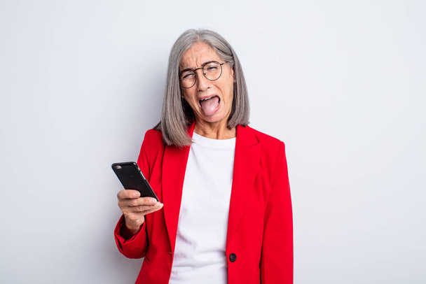 senior pretty woman with cheerful and rebellious attitude, joking and sticking tongue out.. business and phone concept - Foto, Imagem